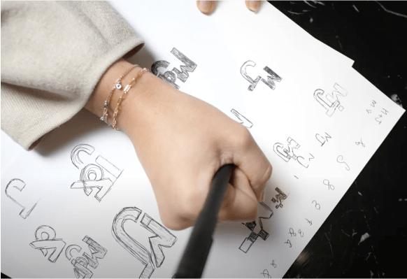 Hand holding pen over paper with drawn logo options