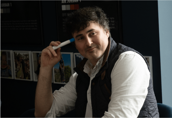 Smiling man with a vest on holding a marker to his head