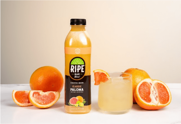 Juice bottle and cocktail glass surrounded by whole and cut grapefruits