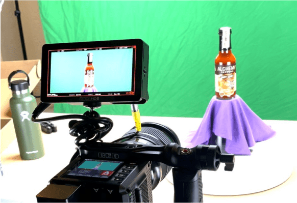 Staged photo of a hot sauce bottle with camera showing and a water bottle on a table