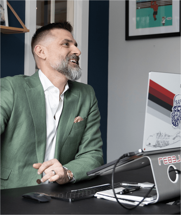 Smiling man with a green blazer on and laptop on desk in front of him